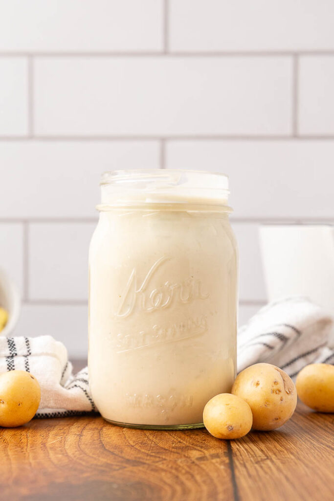 A jar of homemade cream of potato soup with potatoes on the counter.