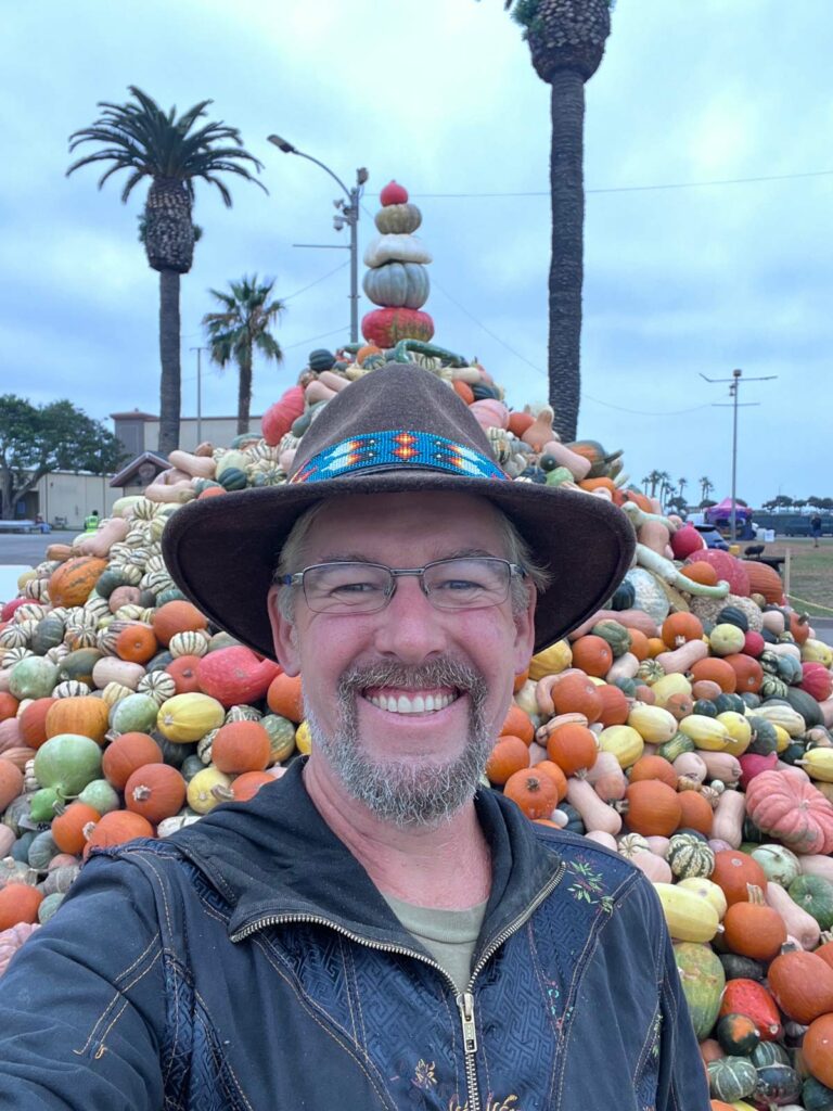 A man in a cowboy hat standing in front of a giant pile of pumpkins.