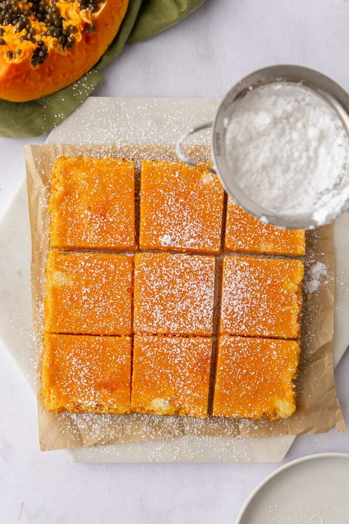 Papaya bars dusted with powdered sugar on a white cutting board.