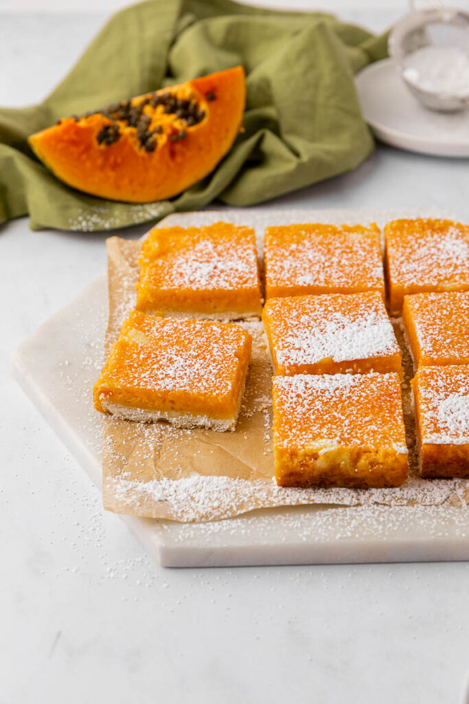 Papaya bars dusted with powdered sugar on a white cutting board.