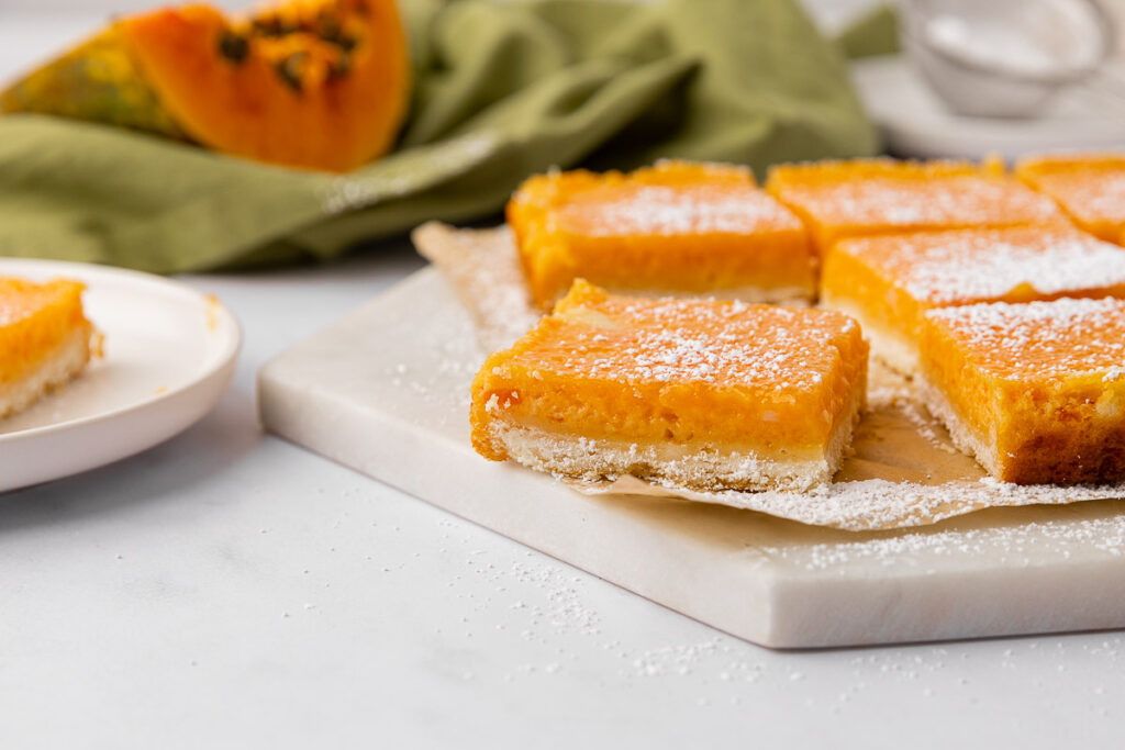 Papaya bars dusted with powdered sugar on a white cutting board.