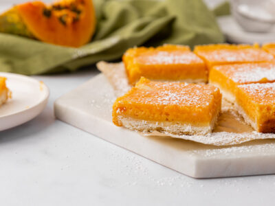 Papaya bars dusted with powdered sugar on a white cutting board.