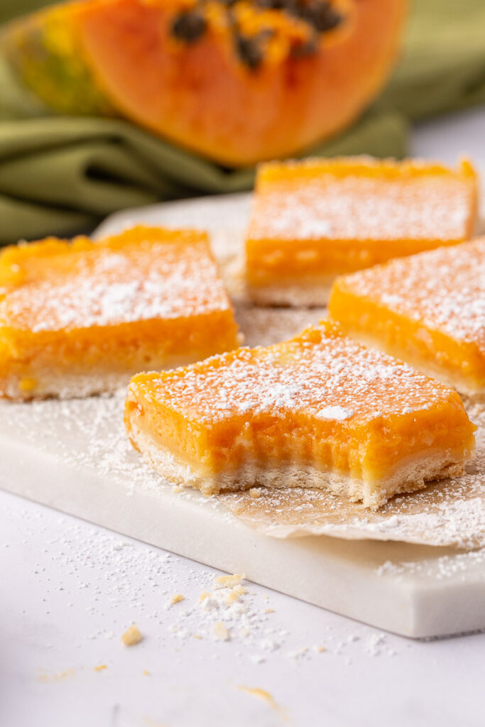 Papaya bars on a white cutting board, one with a bite taken out.