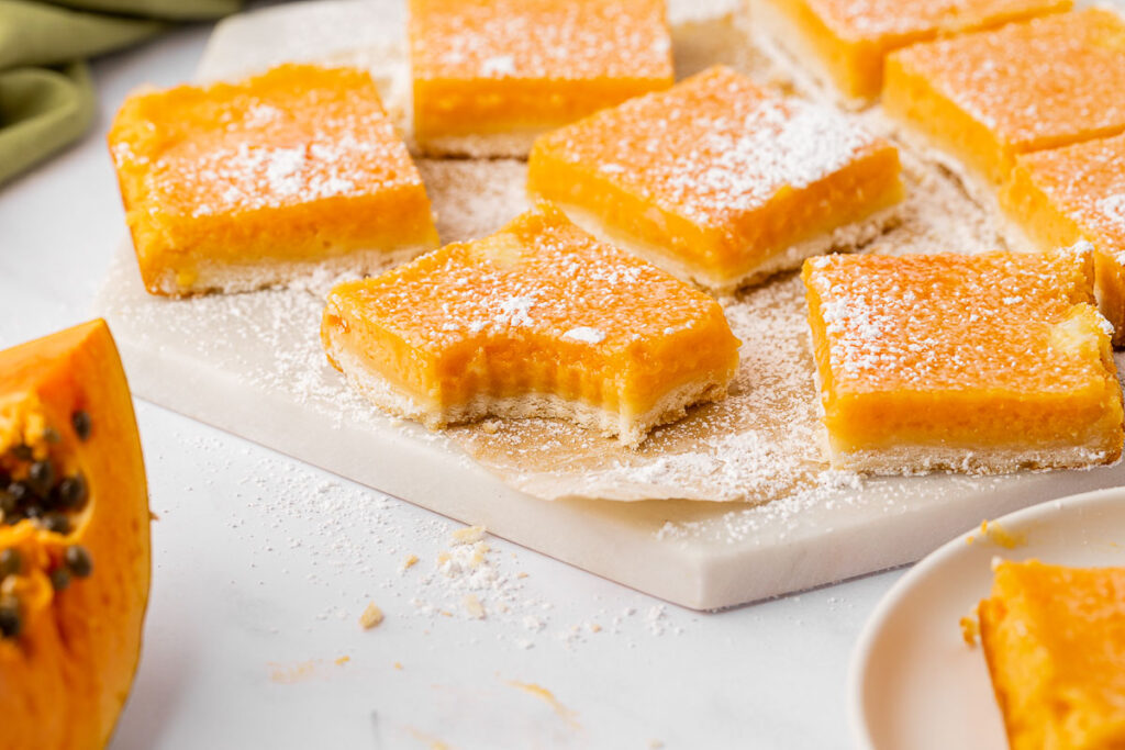 Papaya bars on a white cutting board, one with a bite taken out.