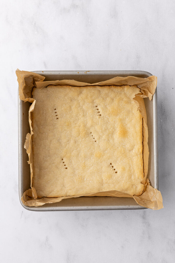 A baked shortbread cookie crust in a square baking pan.