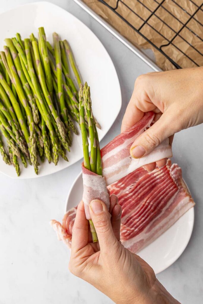 Asparagus being wrapped with bacon.