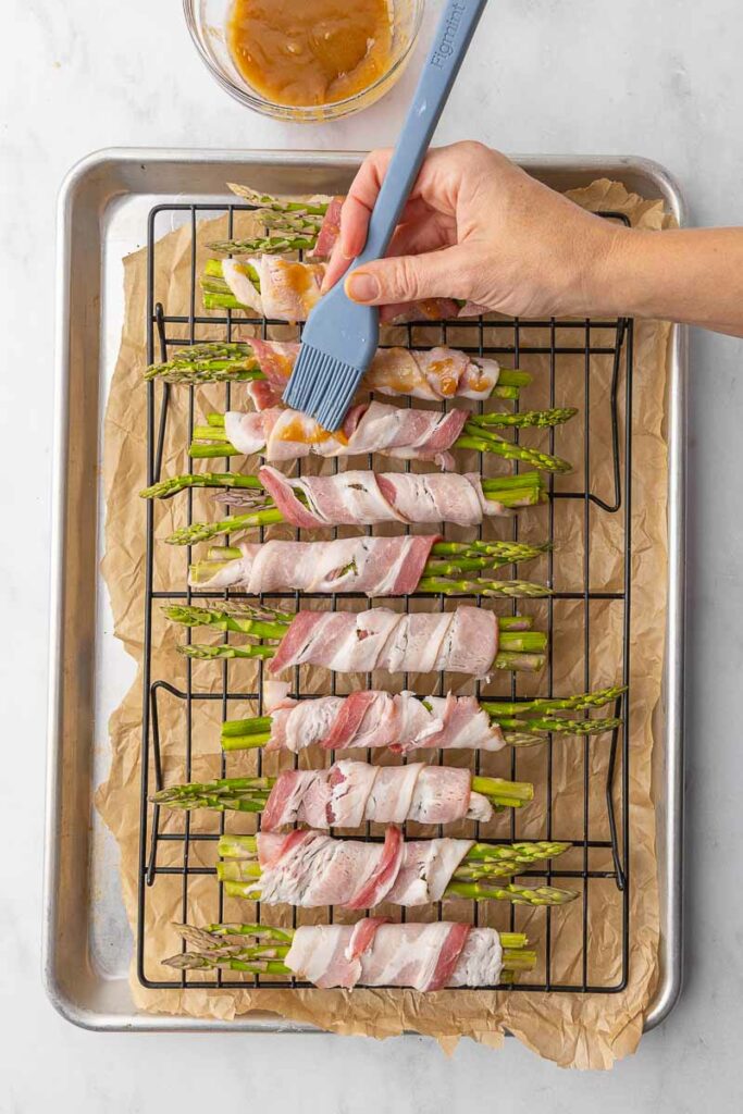 Bacon wrapped asparagus on a wire rack being brushed with brown sugar butter.