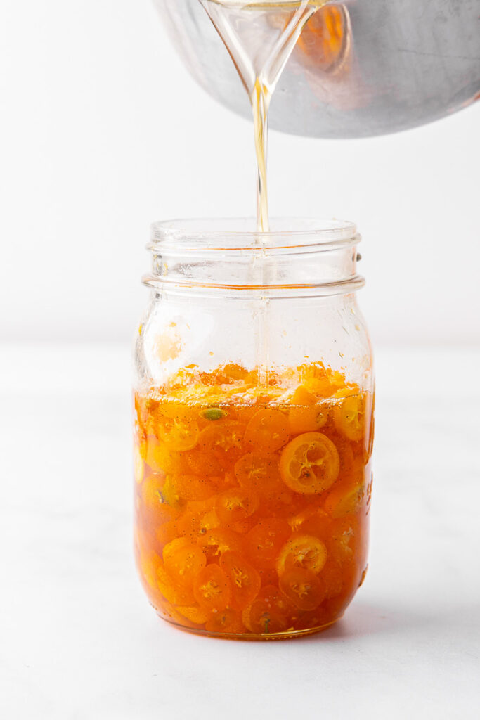 Syrup being poured into a jar of candied kumquats.