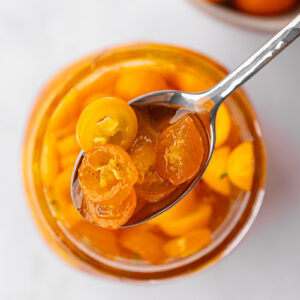 Candied kumquats in a jar with a spoon scooping out.