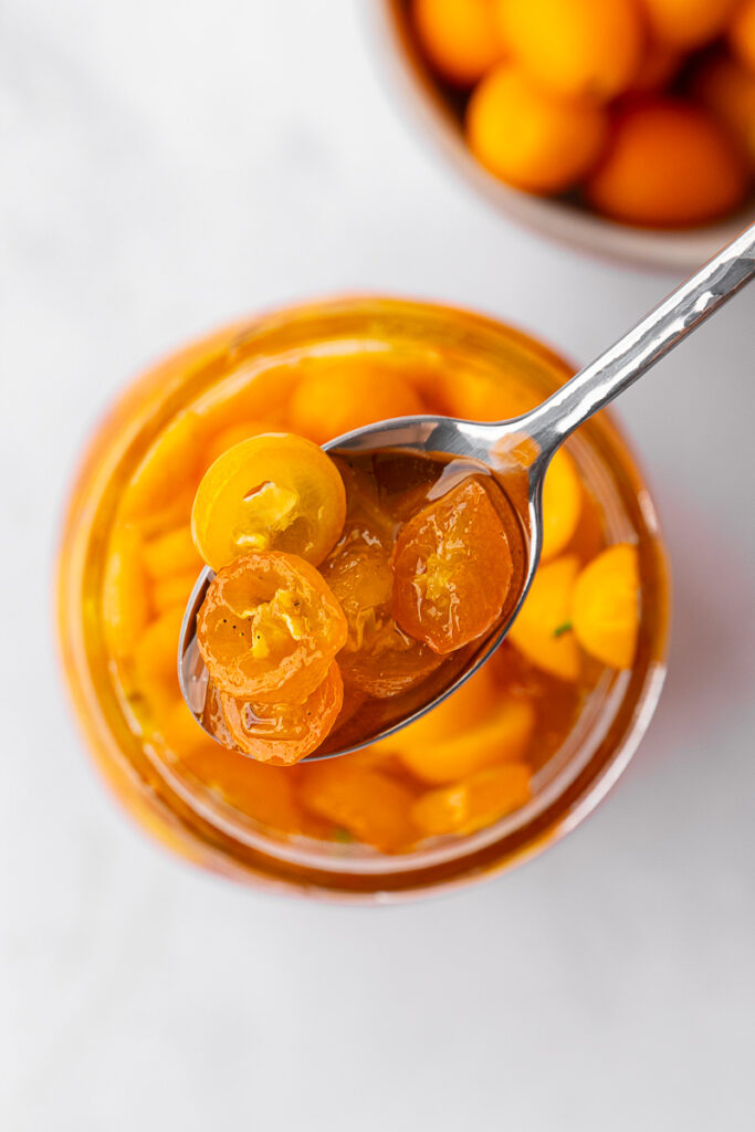 Candied kumquats in a jar with a spoon scooping out.