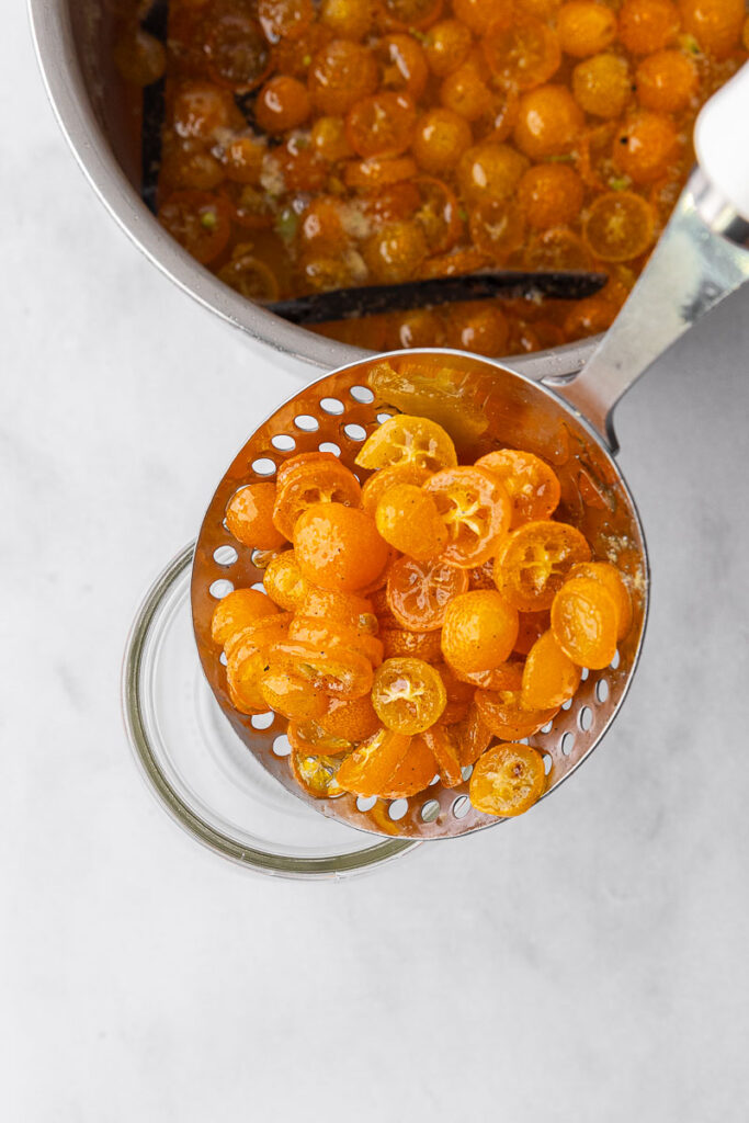 Candied kumquats being scooped into a jar.