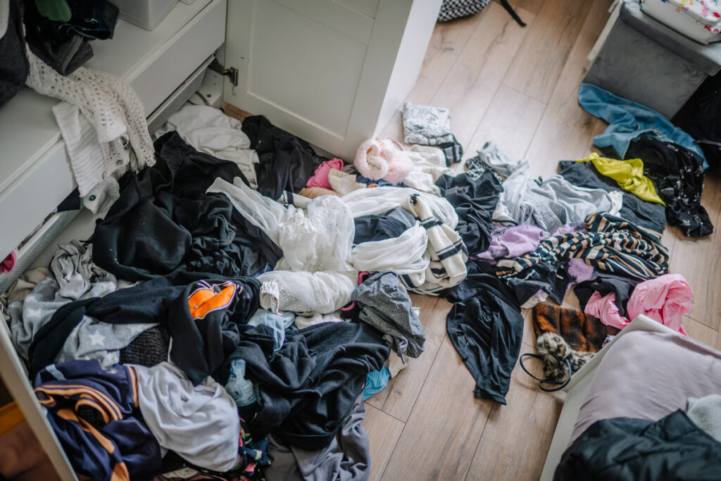 A cluttered closet with clothes all over the floor.