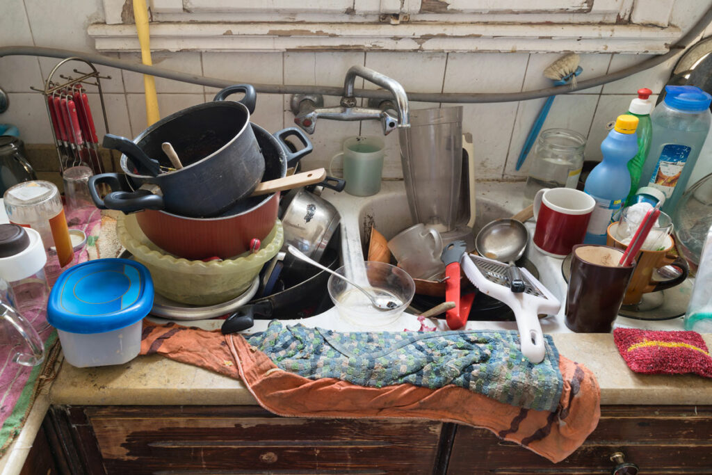 A dirty kitchen with a sink filled with dishes.