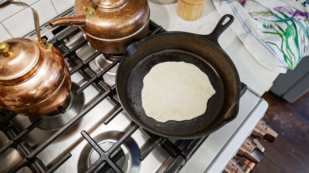 A sourdough tortilla being cooked in a cast iron skillet.