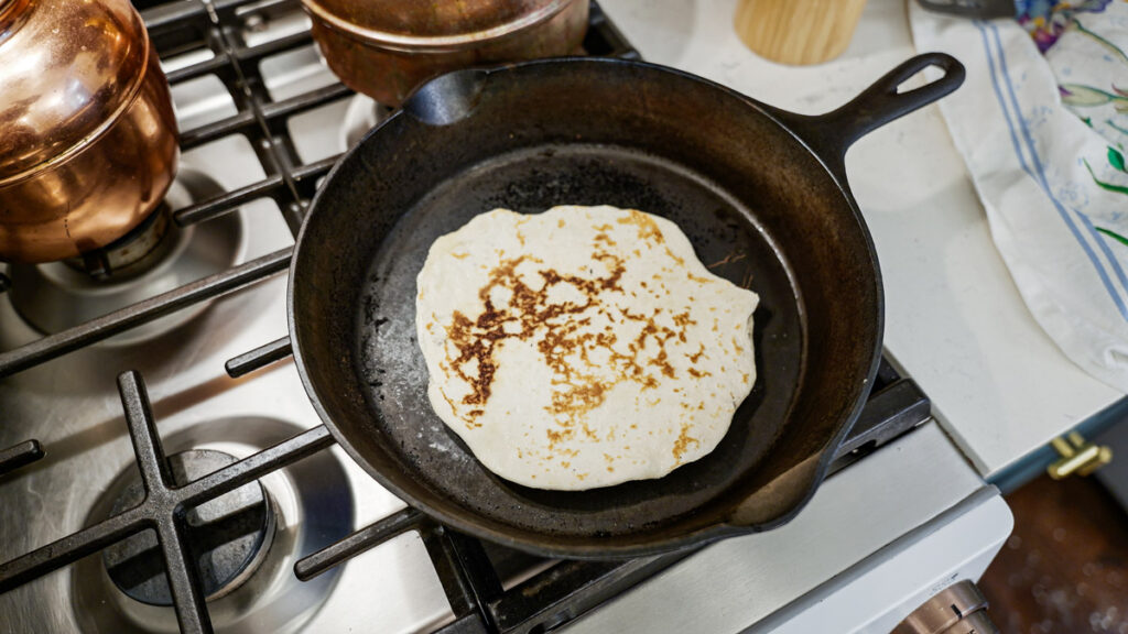 A sourdough tortilla being cooked in a cast iron skillet.