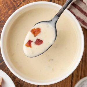 A spoonful of cream of bacon soup with soup in white bowls on a wooden counter.