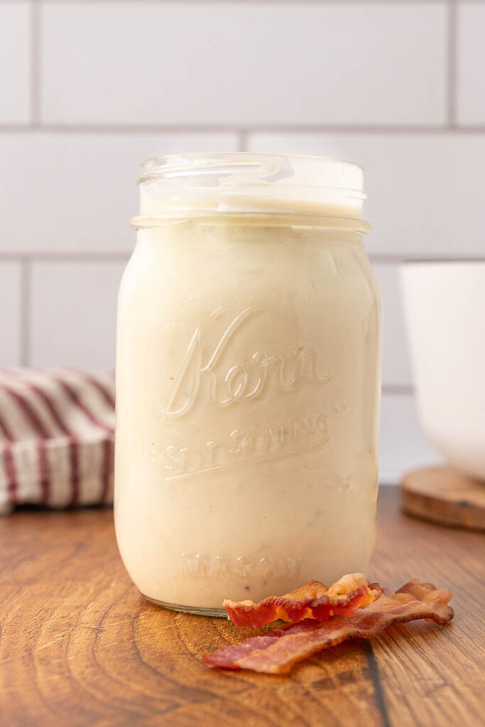 A Mason jar of cream of bacon soup on a wooden counter.