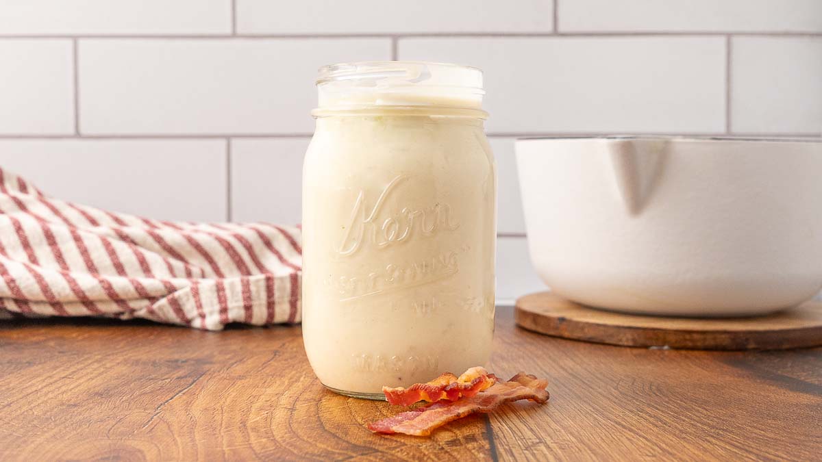 A Mason jar of cream of bacon soup on a wooden counter.