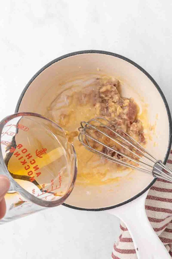 Broth being poured into a base of bacon, butter and flour.