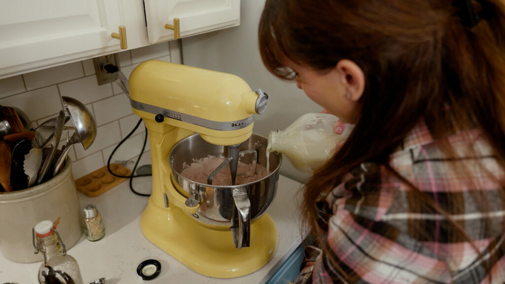 A woman making chocolate frosting in a stand mixer.