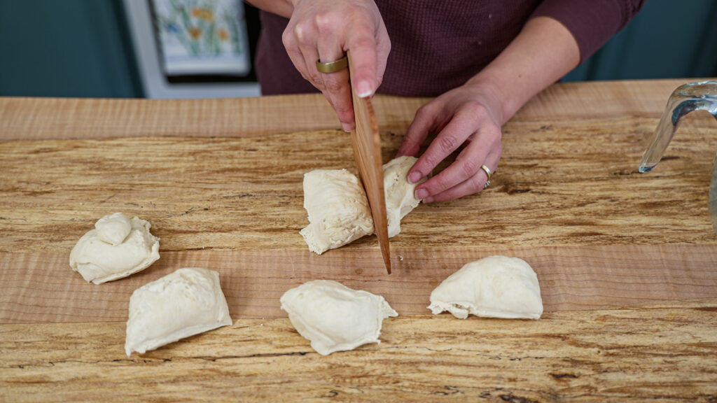 A woman using a wooden bench knife cutting dough into equal portions.