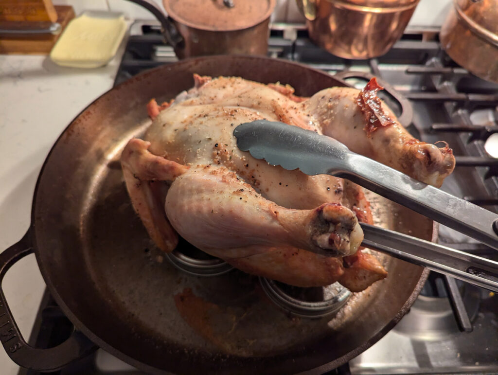 Tongs flipping a roast chicken over so it's breast side up.