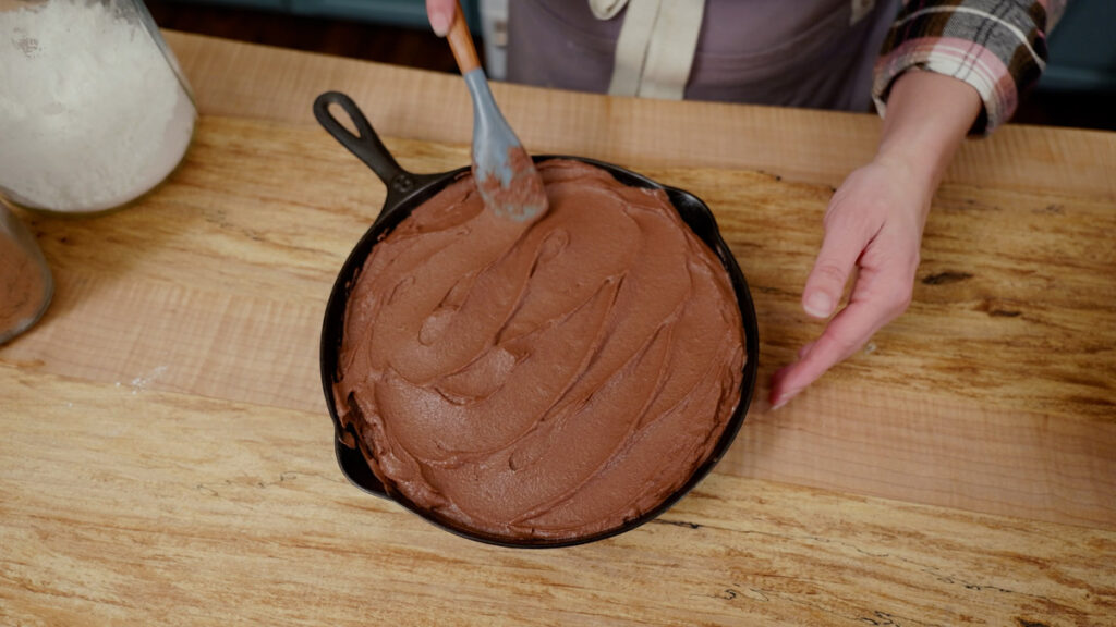 A chocolate cake being frosted with chocolate frosting.