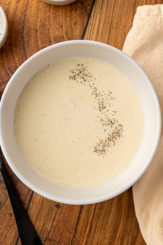 A bowl of cream of gluten free chicken soup on a wooden counter.