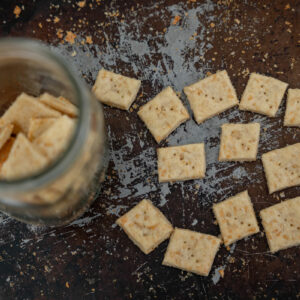 Homemade crackers on a cooking sheet and some crackers in a Mason jar.