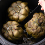 Cooked artichoke being lifted out of an Instant Pot.