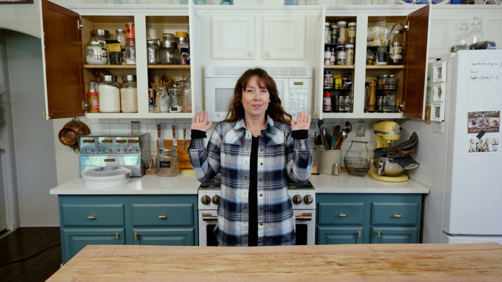 A woman pointing to items in her kitchen cupboard.