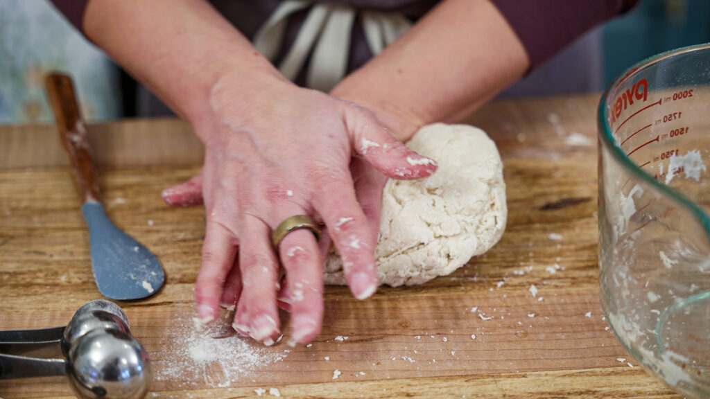 Sourdough tortilla dough being kneaded by hand on a wooden counter.