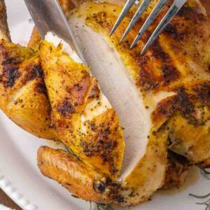 A fork and knife carving a whole roasted chicken.