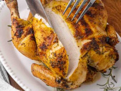 A fork and knife carving a whole roasted chicken.