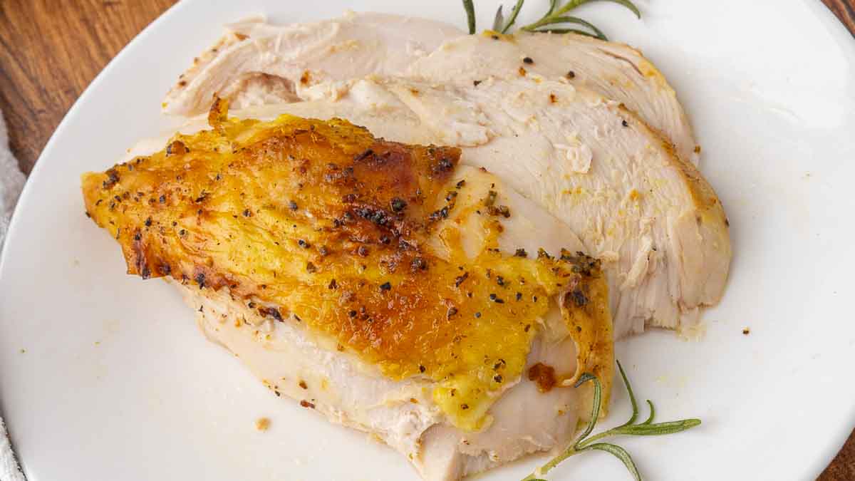 Slices of roasted chicken breast served on a white plate, and garnished with rosemary.