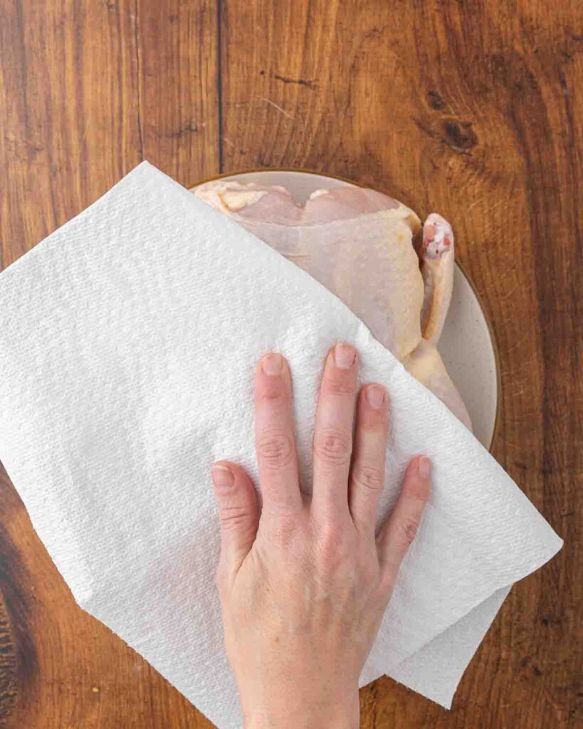 Hands using paper towels to pat a whole raw chicken dry.