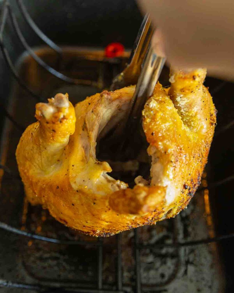 Tongs flipping a whole chicken roasting in the oven.