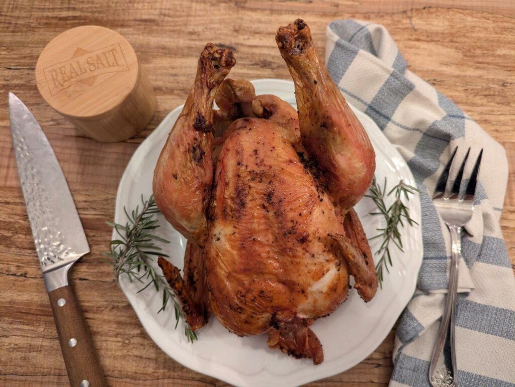 A cooked whole roast chicken on a white serving platter.