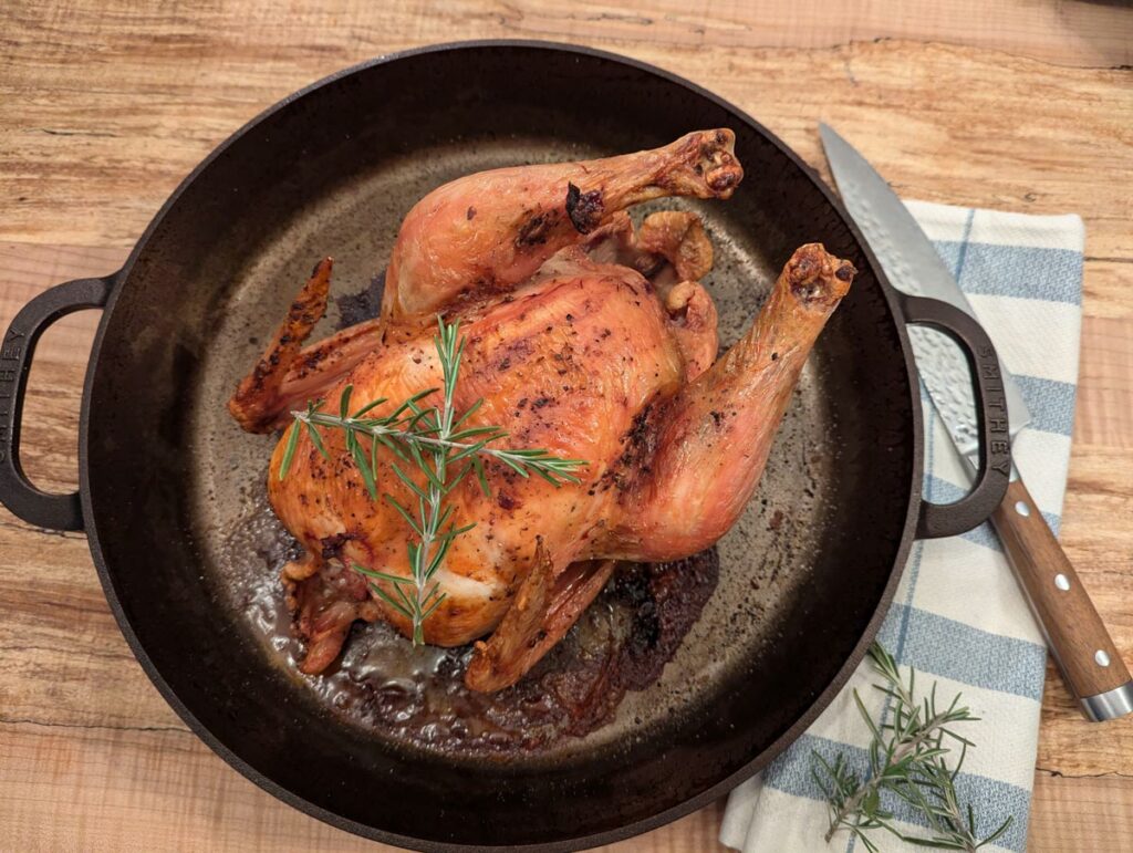 A cooked whole roast chicken in a cast iron skillet.