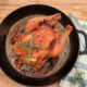 A cooked whole roast chicken in a cast iron skillet.