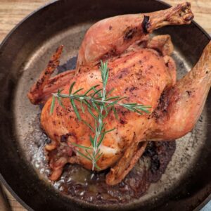 A cooked whole roast chicken in a cast iron skillet.