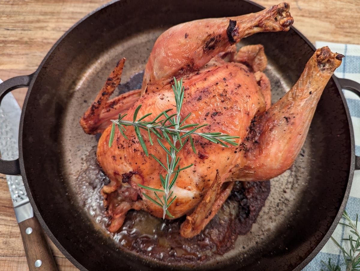 A cooked whole roast chicken in a cast iron skillet.