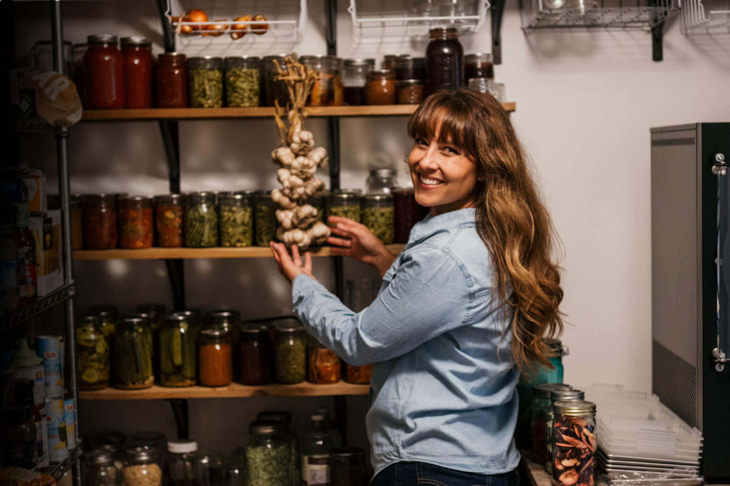 Melissa in Pantry with braid of garlic and jars of home canned food