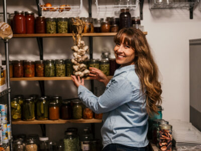 Women holding a braid of garlic infront of rows of home canned food