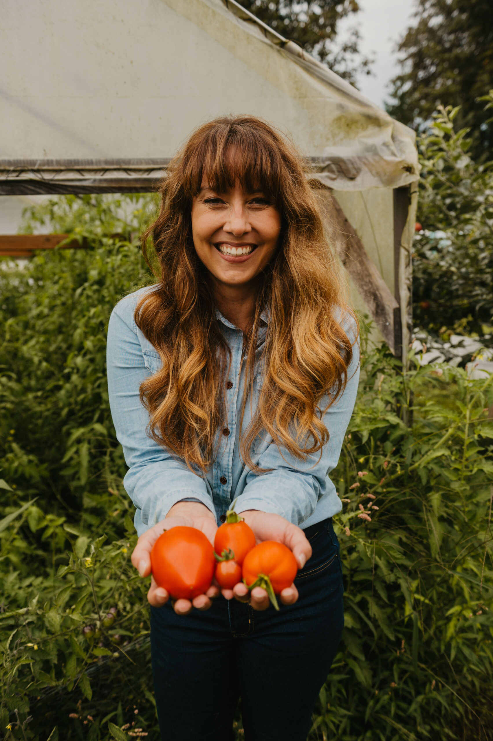 A woman holding up two home-grown tomatoes.