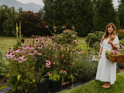 Woman barefoot in herb garden holding a basket of freshly harvested flowering herbs