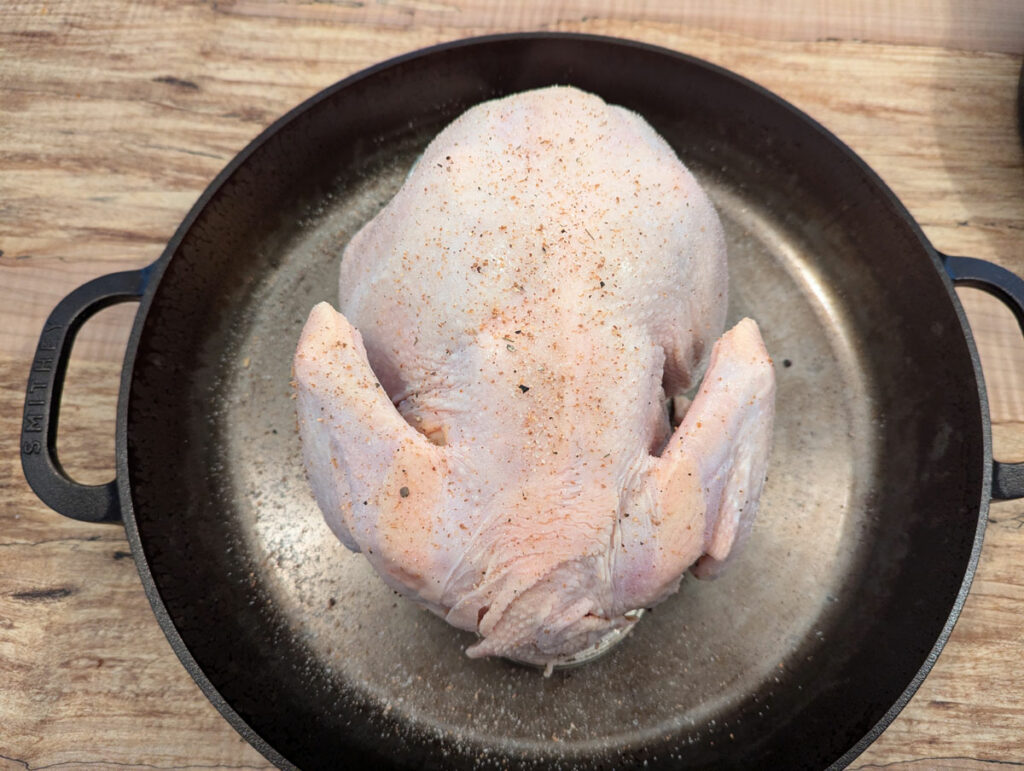 An uncooked chicken, breast side down in a cast iron pan.