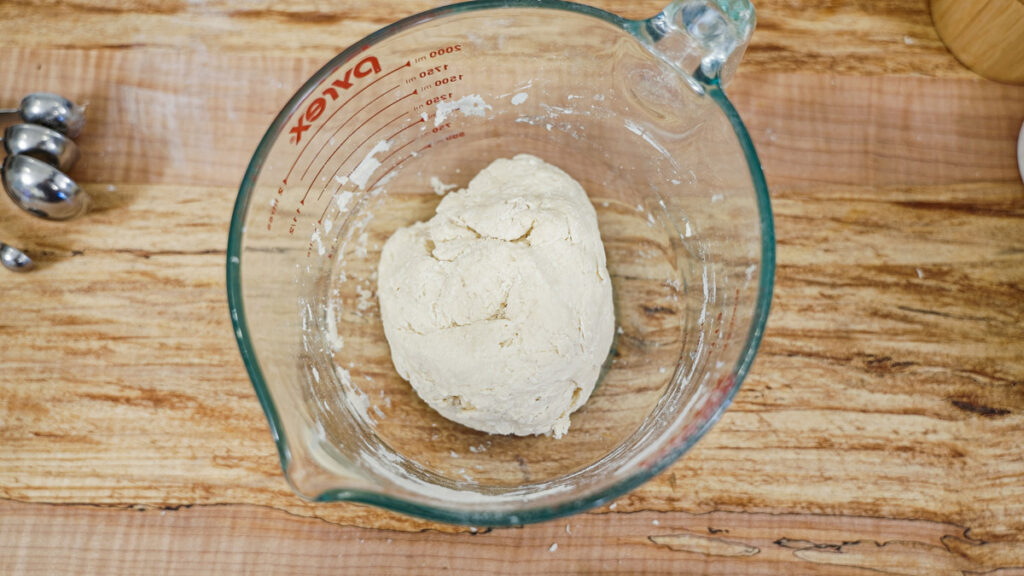 Sourdough tortilla dough resting in a glass bowl.