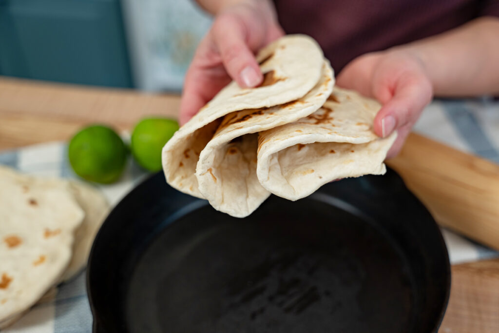 A woman holding a stack of sourdough tortillas all folded in half.