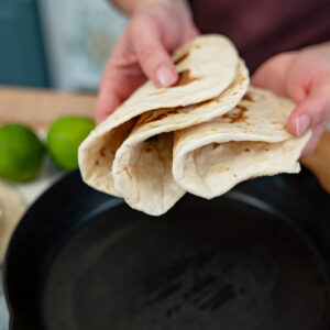 A woman holding a stack of sourdough tortillas all folded in half.